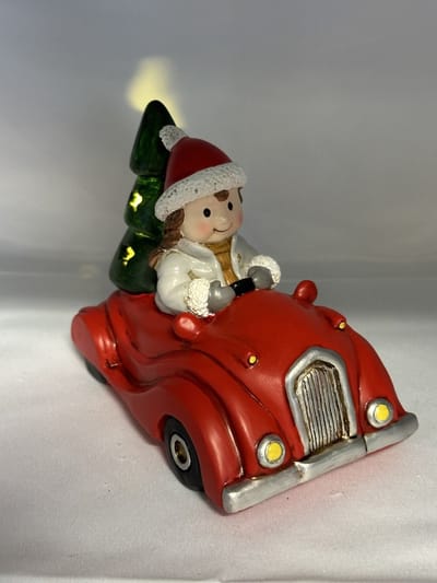 Kerstbeeldje meisje in rode auto met LED - grijs vest + groene kerstboom - polyresin - 12 cm hoog x 16 cm x 8 cm – Kerstdecoratie