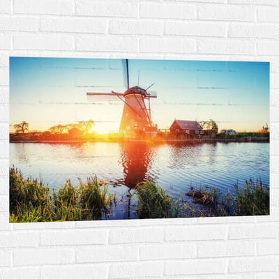 WallClassics - Muursticker - Zonlicht langs Hollandse Molen aan het Water - 105x70 cm Foto op Muursticker