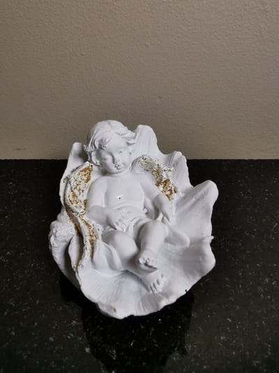 Slapend engeltje-cherubijntje met lange vleugels met gouden glittertjes ligt te slapen in een schelp