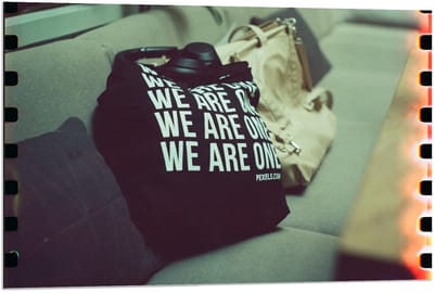 Dibond - Bank met Tassen en Tekst We Are One - 90x60cm Foto op Aluminium (Met Ophangsysteem)