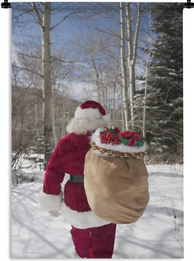 Wandkleed Kerst - De kerstman loopt met een zak vol met kerstcadeaus door een bos Wandkleed katoen 90x135 cm - Wandtapijt met foto