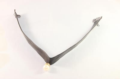 Zwarte kunstleren choker met parel gezet in een houder met kristalletjes.