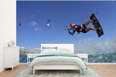 Behang - Fotobehang Vrouw vliegt over de golven met haar kiteboard. - Breedte 295 cm x hoogte 220 cm