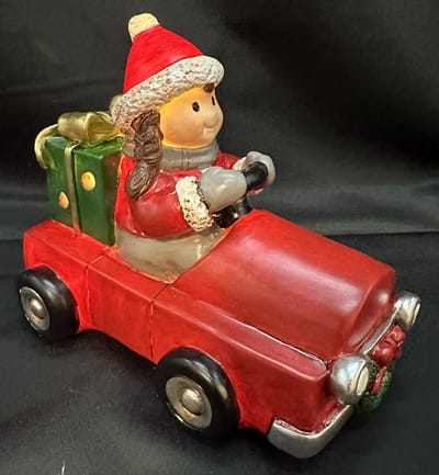 Kerstbeeldje meisje in rode auto met LED - rode trui + groen cadeau - polyresin - 12 cm hoog x 16 cm x 8 cm – Kerstdecoratie