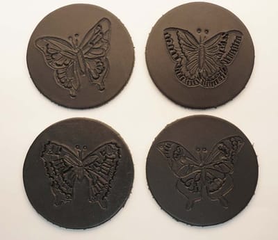 Zwarte ronde 100% leren onderzetters 4 verschillende vlinders set van 4 stuks - mooie fladderende onderzetters - fleurige onderzetters - vlinders onderzetters - butterfly onderzetters van leer - zwarte handmade onderzetters - vlindertjes onderzetters