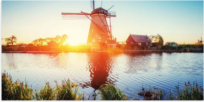 WallClassics - Poster Glanzend – Zonlicht langs Hollandse Molen aan het Water - 100x50 cm Foto op Posterpapier met Glanzende Afwerking