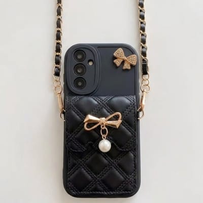 Zwart telefoon hoesje – geschikt voor Samsung Galaxy S25– backcover voor dames – doorgestikt lederlook design – goudkleurige strik met parel – hoesje met schouderkoord